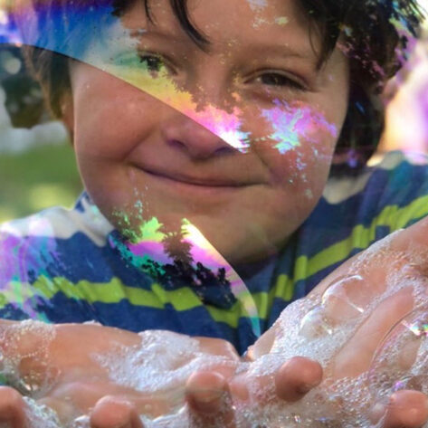 a young boy holding a large soap bubble with soap on his hands at thePatriotic Festival