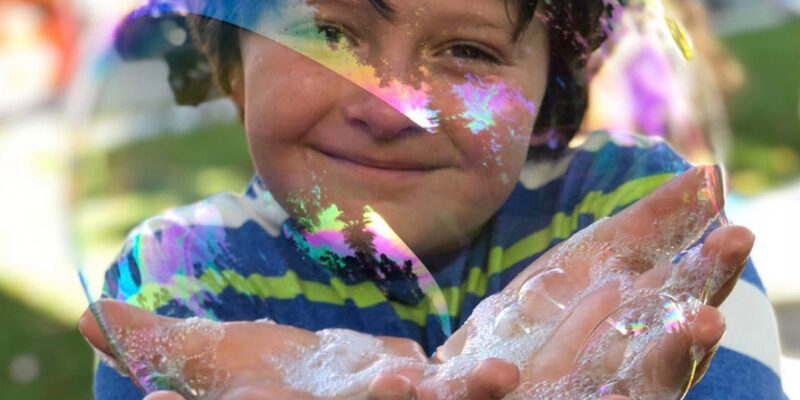 a young boy holding a large soap bubble with soap on his hands at thePatriotic Festival