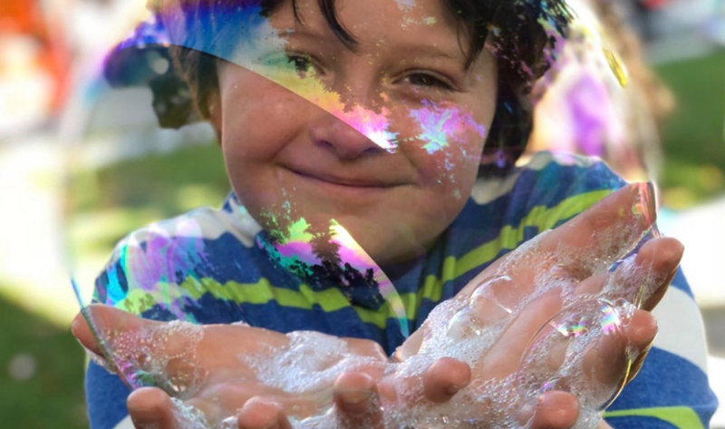 a young boy holding a large soap bubble with soap on his hands at thePatriotic Festival