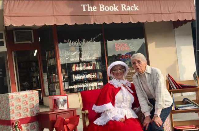 a woman in a Mrs Clause outfit seated with another woman outside a bookstore