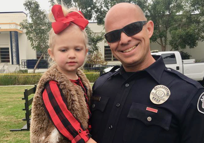 a man in a police officer's uniform holding a young girl wearing a fur vest witha red bow