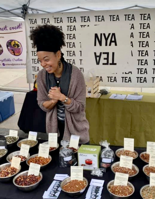 a woman at a booth of tea with loose tea leaves on a table in front of her
